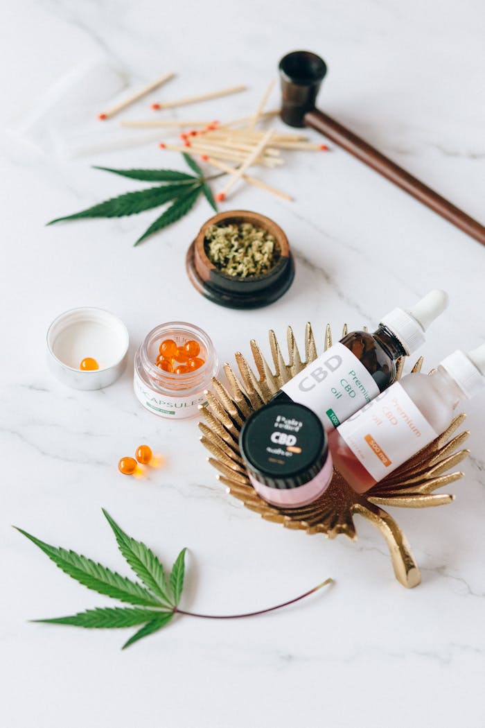 Top view of CBD oil bottles, capsules, hemp leaves, and pipe on marble.